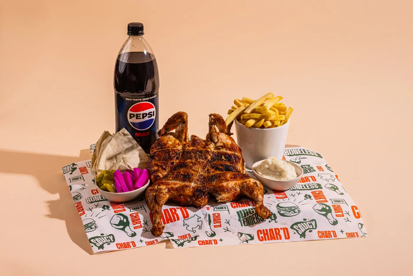 Whole charcoal chicken with chips, pickles, garlic sauce, salad and a drink on Char’d paper