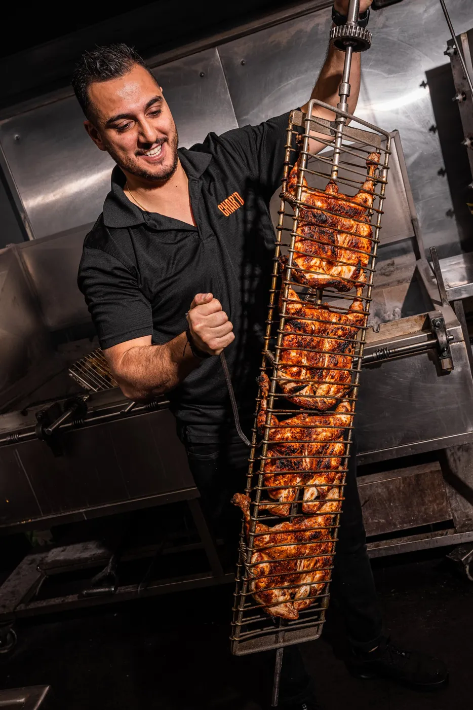 Char’d cook lifting a full rack of chickens off the charcoal pit